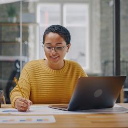 A person in a yellow sweater is completing work in front of a laptop