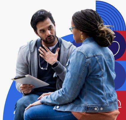 A medical professional is holding a medical chart and talking with a patient who is wearing glasses. 