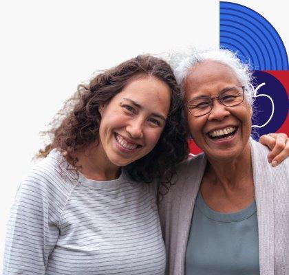 A younger woman smiles and places her arm around a laughing older woman.