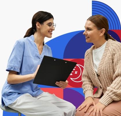 A female clinician with dark hair and glasses smiles while reviewing medical information with a smiling female patient with light brown hair wearing a chunky beige sweater.