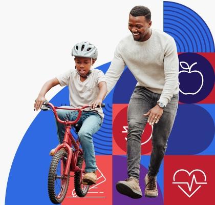 A young Black man smiles while helping his son ride a bike.