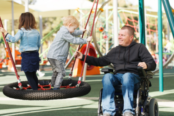 Man in wheelchair pushing children on tire swing