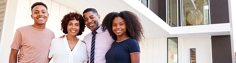 A mother and father with 2 teenage children pose for the camera in front of their home.