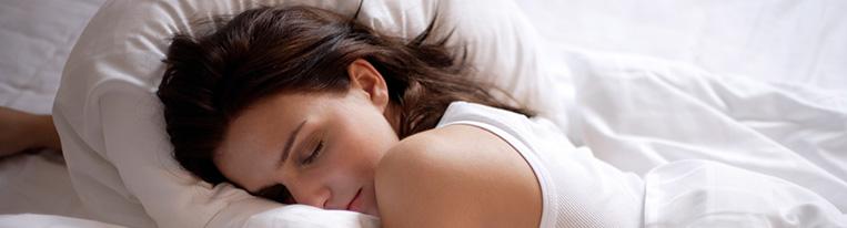 A woman sleeps on white bed linens.