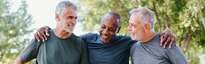 Three older men wearing athletic gear smile with arms over each other's shoulders.