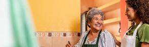 An older woman smiles at a younger woman as they cook together.