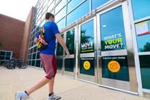 A person wearing a blue short sleeved shirt and purple gym shorts walking toward a door that says, “What’s your move?” on the University of Maryland campus.