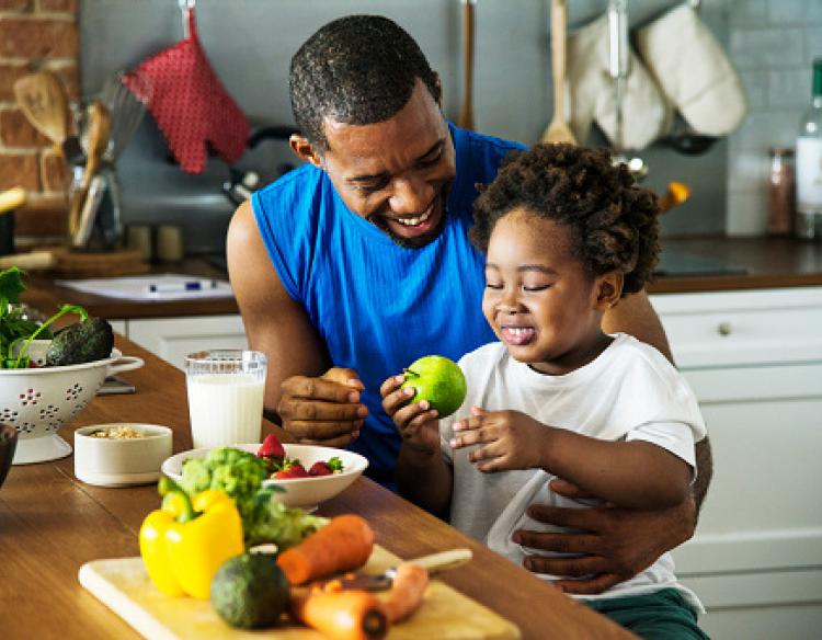 Father and child sitting down with a meal of fresh produce.