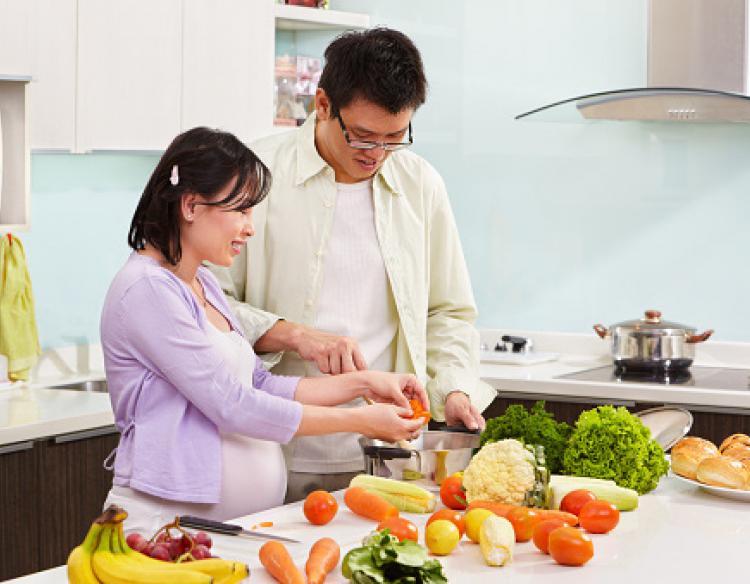 A man and pregnant woman preparing healthy produce for a meal.