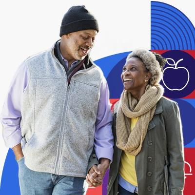 Dos adultos mayores de raza negra, un hombre y una mujer, caminan y sonríen tomados de la mano.