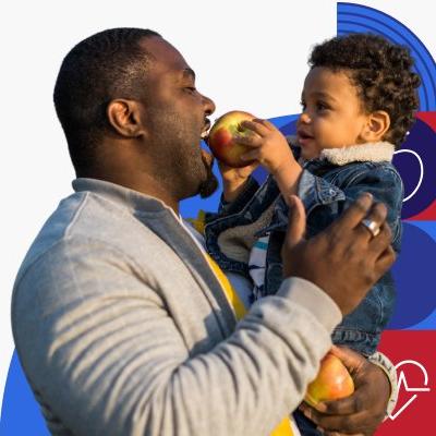 Un padre de raza negra comparte una manzana con su hijo pequeño.