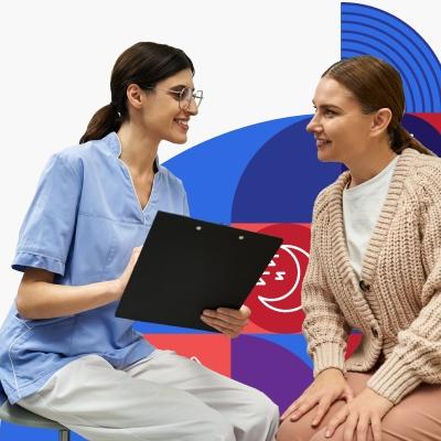 A female clinician with dark hair and glasses smiles while reviewing medical information with a smiling female patient with light brown hair wearing a chunky beige sweater.