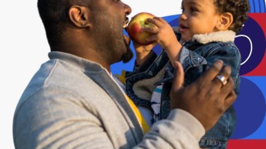 Un padre de raza negra comparte una manzana con su hijo pequeño.